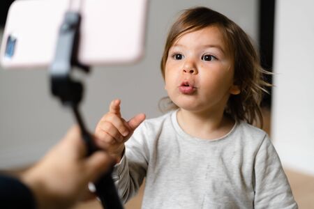 Toddler girl using phone with selfie stick to call grandparents. Virtual connection of peopleの写真素材