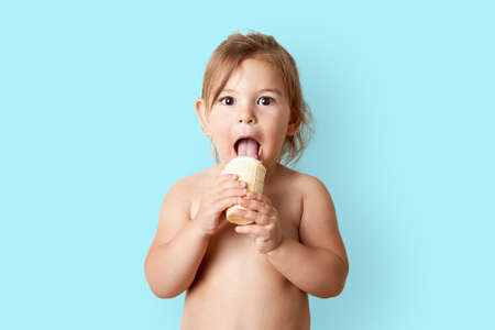 Child eating ice cream in studio shot. Funny happy toddler with summer foodの写真素材
