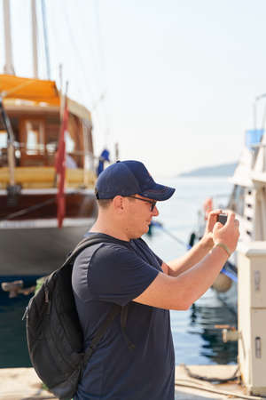 Portrait of caucasian man with backpack making photo on smartphone. Yachting seaside travel.の写真素材