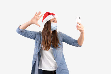 Young woman with phone medical mask and santa hat. Christmas shopping online on quarantine.の写真素材