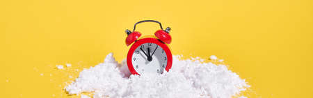 Red retro alarm clock with snow on yellow background. Creative Christmas or New year concept.の写真素材