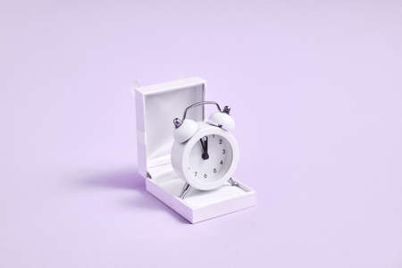 Jewelry white box and alarm clock in it. Waiting for marriage proposal. New year midnight propose.