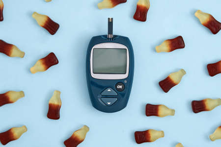 Top view of glucose meter and sweet jelly candies on blue background. Diabetes, high blood sugar...
