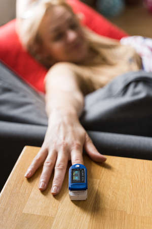 Middle age woman at home checking blood oxygen level with pulse oximeter.  Asthma, lungs decease.
