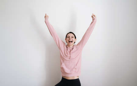 Millennial young woman in pink hoodie on white background. Women empowerment concept. Hands up happy woman. Feminism superwoman portraitの写真素材