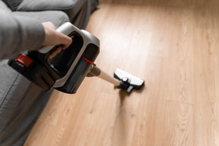 Cleaning wooden floor with wireless vacuum cleaner. Handheld cordless cleaner. Household appliance. Housework modern equipmentの写真素材