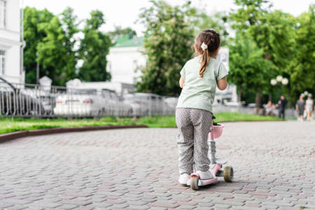 Preschool happy girl riding pink mini scooter in European city. Summer outdoors activities for kids. No helmet safety risk. Toddler play in urban areas. Sustainable parentingの写真素材