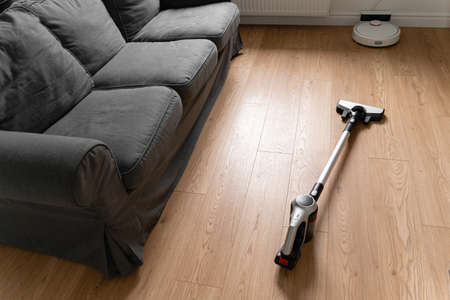 Cleaning wooden floor with wireless vacuum cleaner. Handheld cordless cleaner. Household appliance....