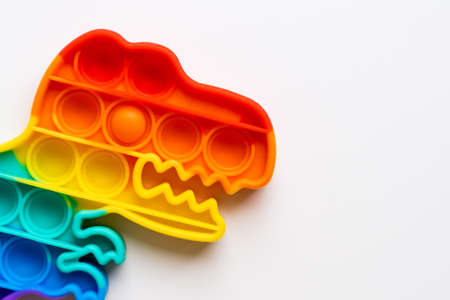 Popit rainbow toy in rainbow colours and dino shape. Trendy bubble pop fidget. Funny anti stress sensory trend. White background and finger popping the bubbles.の写真素材