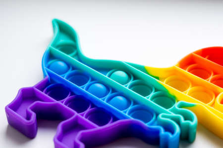 Popit rainbow toy in rainbow colours and dino shape. Trendy bubble pop fidget. Funny anti stress sensory trend. White background and finger popping the bubbles.の写真素材