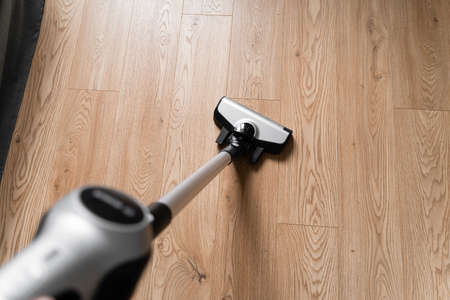 Cleaning wooden floor with wireless vacuum cleaner. Handheld cordless cleaner. Household appliance. Housework modern equipmentの写真素材