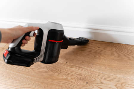 Cleaning wooden floor with wireless vacuum cleaner. Handheld cordless cleaner. Household appliance. Housework modern equipmentの写真素材