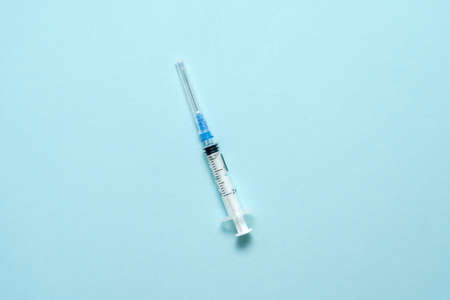 Top view of injection syringe on blue background. Minimal vaccine concept. Medical treatment of...