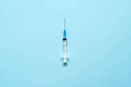 Top view of injection syringe on blue background. Minimal vaccine concept. Medical treatment of...