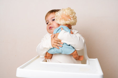 Baby toddler hugs with old-fashioned doll on a studio shot. Funny serious face. Best friend toy. Role independent play of toddler. Montessori educationの写真素材