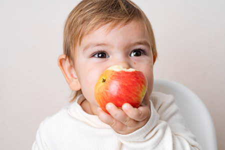 Toddler baby with apples on the high chair. Healthy eating. Summer and autumn harvest. Studio shotの写真素材