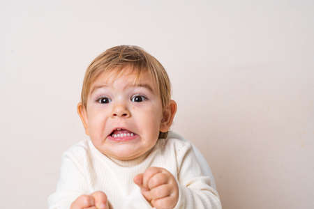 Toddler baby sitting on the high chair and doing funny grimace. Teeth of the baby. Face expressionの写真素材