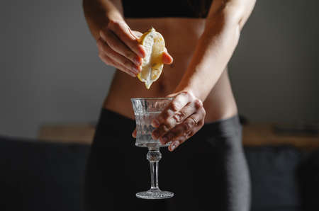 Close up of young fit slim woman preparing water with lemon juice. Morning ritual. Healthy antioxidant. Slimming diet. Boost immunity and metabolismの写真素材