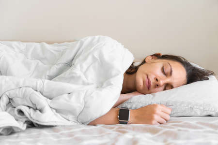 Young woman goes to sleep Phone addiction, insomnia. try to fall asleep. Sleep tracking on the phone and smart watch. Circadian rhythm.の写真素材