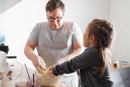 Father feeling playful with his caucasian little daughter, while preparing homemade dough for tasty cookies. Father and his child spending time at homeの写真素材