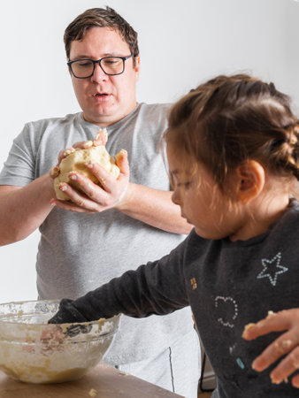 Father feeling playful with his caucasian little daughter, while preparing homemade dough for tasty cookies. Father and his child spending time at homeの写真素材