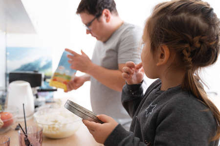 Father feeling playful with his caucasian little daughter, while preparing homemade dough for tasty cookies. Father and his child spending time at homeの写真素材