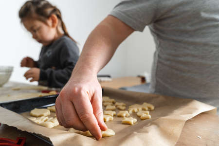 Cropped view of unrecognizable man and his daughter making sweets with biscuit cutters on processing...