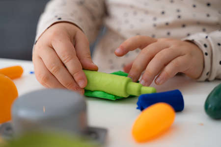 Close up view of the little kid girl sitting at the table and toying with colored figures. Concept...