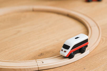 Toddler girl in white dress plays with wooden train at home in the living roomの写真素材