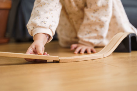 Toddler girl in white dress plays with wooden train at home in the living room