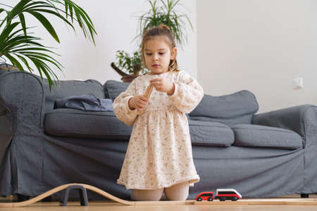 Toddler girl in white dress plays with wooden train at home in the living roomの写真素材