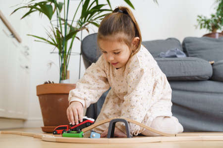 Toddler girl in white dress plays with wooden train at home in the living roomの写真素材