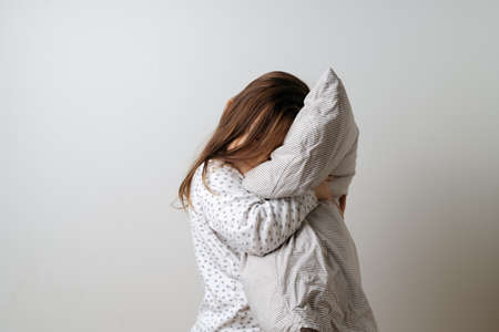 Portrait of pretty caucasian girl in white pyjama and pillow in studio white backgroundの写真素材