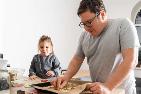Cropped view of unrecognizable man and his daughter making sweets with biscuit cutters on processing board. Father putting cookies on the baking sheetの写真素材