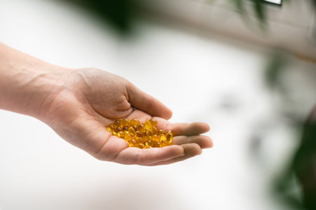 Close up of hand full of yellow softballs. Taking supplements, vitamin D or omega. Wellbeing biohacking conceptの写真素材