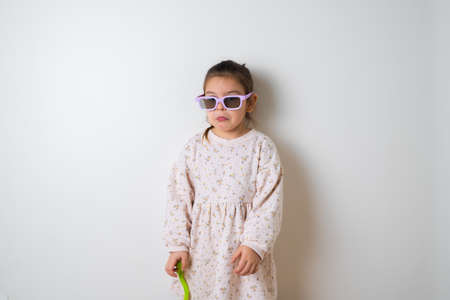 Toddler girl in sunglasses play with toy flower on white backgroundの写真素材