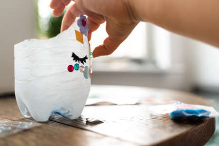 Caucasian preschool girl doing crafts with plastic bottle and paints. Recycle upcycling waste. Sustainable lifestyleの写真素材