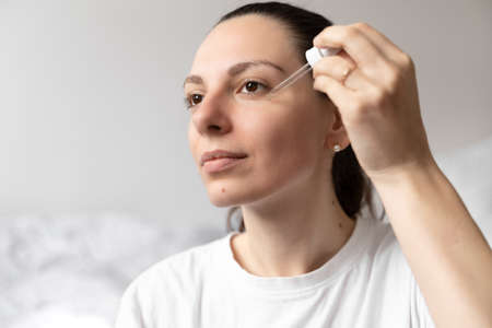 Close up of white woman hand applying oil of essential oil or serum for skin. Self care concept