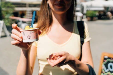Close up of teen girl with paper cup with mango yellow sorbet ice cream on sunny summer day