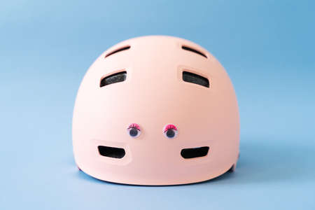 Pink helmet with funny doll eyes on blue background. Childs outdoors activity safety protectionの写真素材