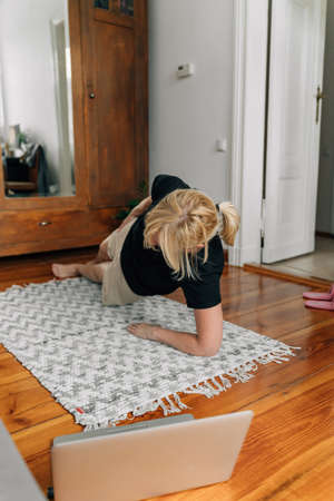mature woman at home doing sport yoga on the floor with laptop online classes