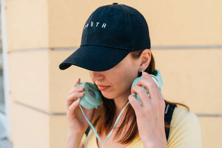 Young woman with mint headphones and black cap outside on the street.の写真素材