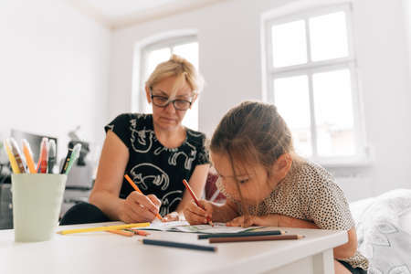 Mature woman granny with grandchild preschool girl drawing together at home.の写真素材