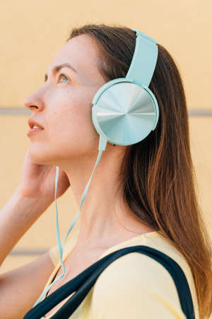 Young woman with mint headphones and black cap outside on the street.の写真素材