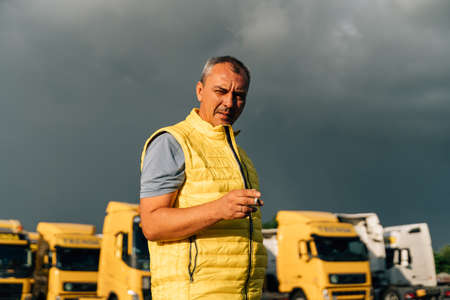Mature middle age man standing at trucks parking and talking on sunny day. Manager of warehouse or driverの写真素材