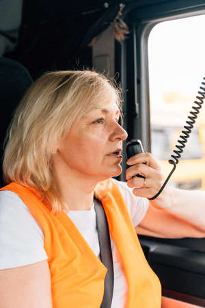 Woman truck driver talking by radio inside the cabin. Female trucker job workerの写真素材