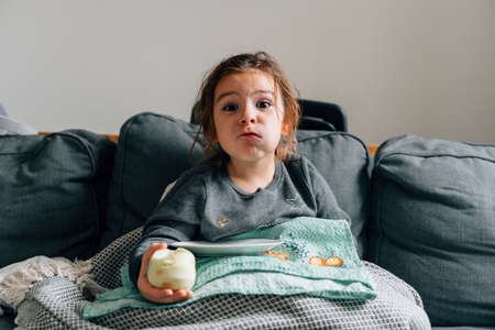 Caucasian preschool girl eating apple on the sofa in living room