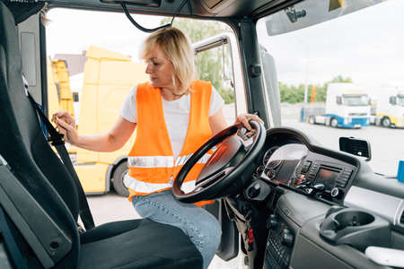 Mature woman truck driver steering wheel inside lorry cabin. Happy middle age female trucker...