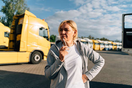 Caucasian mature woman in middle age working as a truck driver. Smoking on a parking lot of trucksの写真素材