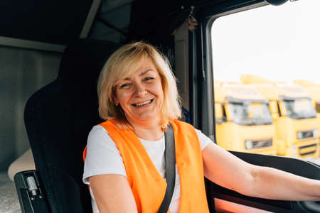 Mature woman truck driver steering wheel inside lorry cabin. Happy middle age female trucker...
